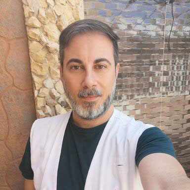 Photo of man with grey hair and beard wearing a white vest over a dark t-shirt